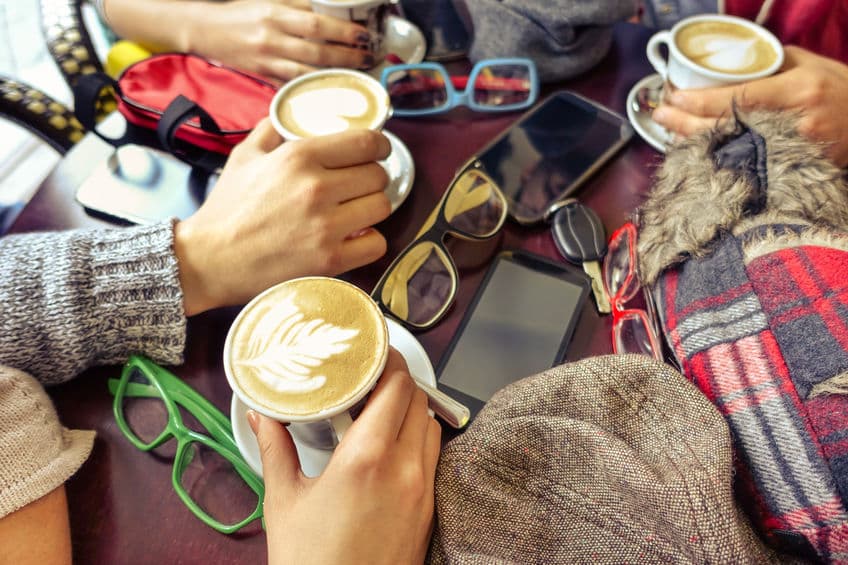 hands holding capuccino cup group of friends having fun in caf